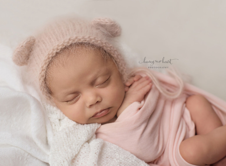 Baby girl wrapped in pink wearing angora bear bonnet and posed newborn photography studio session