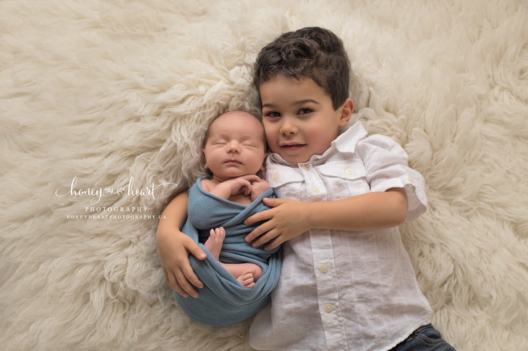 3 year old big brother holding baby brother laying down sibling poses - newborn photography Calgary baby pictures