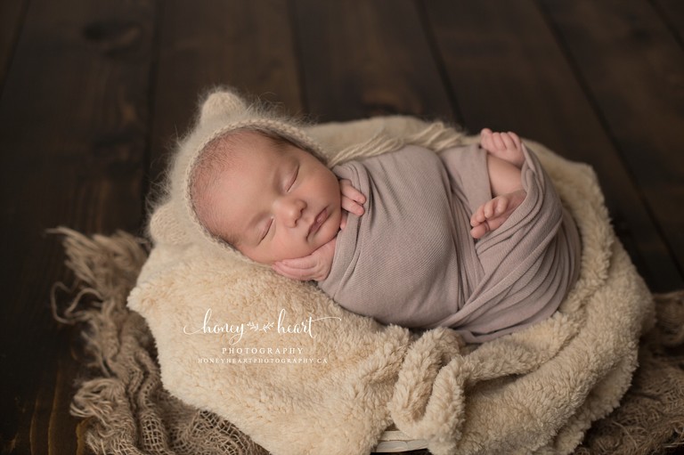Baby boy wrapped laying in wooden bowl with fuzzy layer and softened burlap layer - Calgary Newborn Baby Photographer