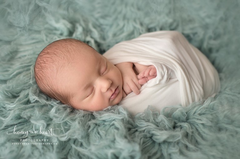 Newborn infant swaddled in cream colored wrap laying on Luneberry's Dutch Blue Flokati - Newborn Photographer Calgary AB