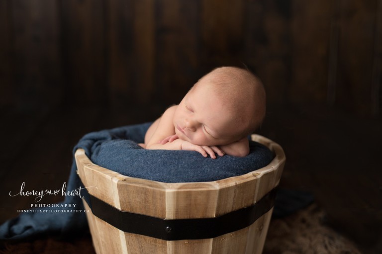 Newborn baby boy sleeping in rustic bucket with blue wrap