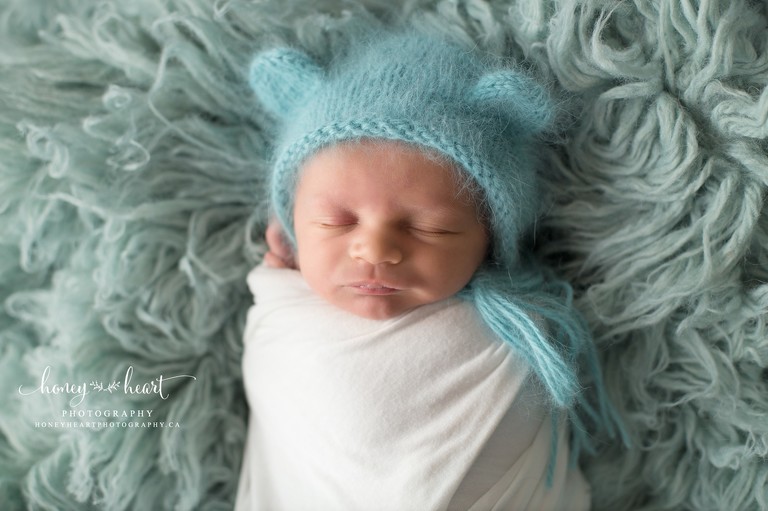 Baby boy wrapped up on dutch blue flokati wearing knitted bear bonnet in blue