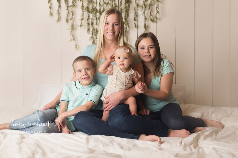 Mom sitting on a bed with her three children studio photography session Calgary family photographer