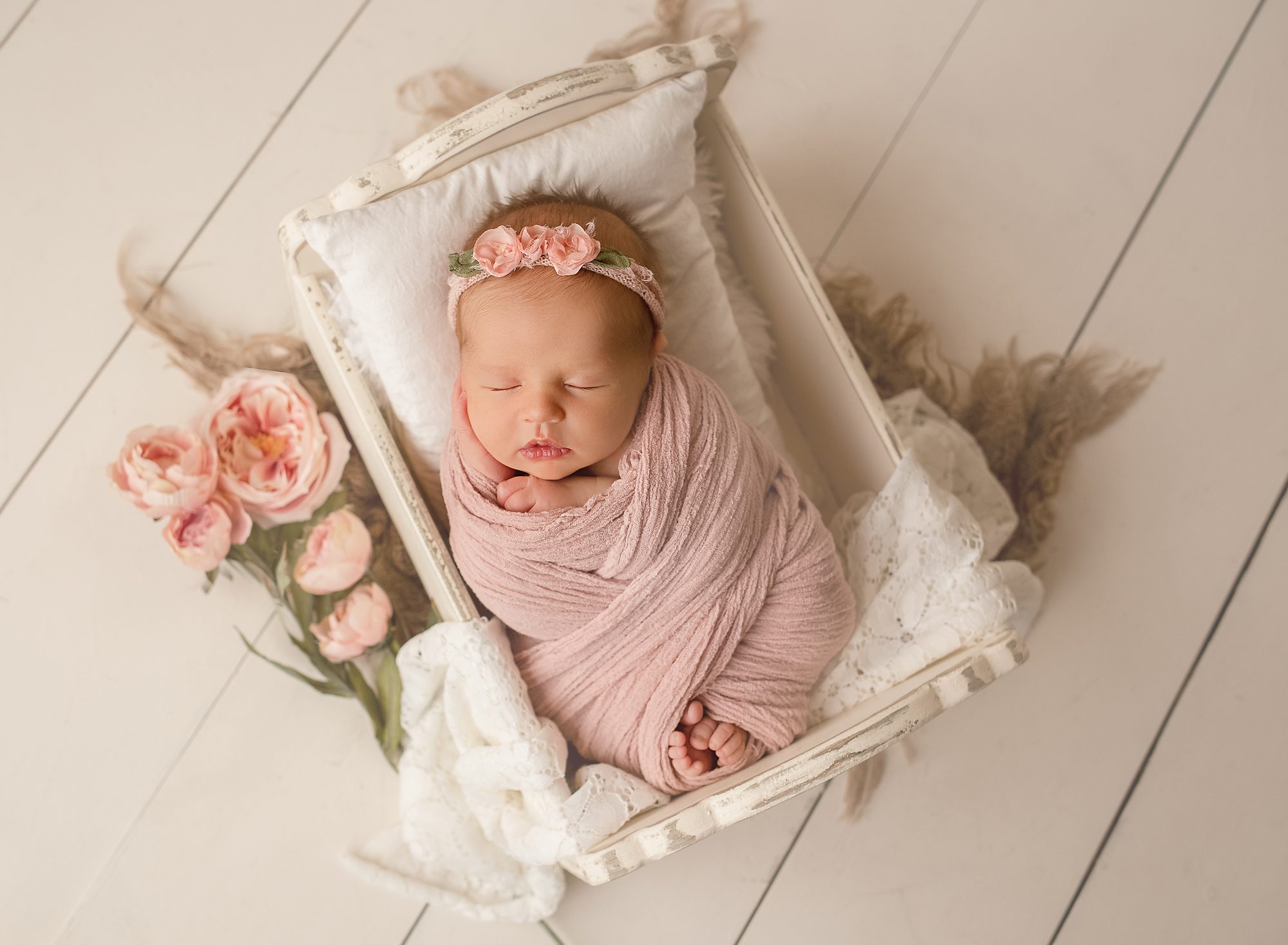 newborn baby girl wrapped in pink wrap wearing pink flower headband posed in wooden newborn photoshoot prop newborn photography Calgary